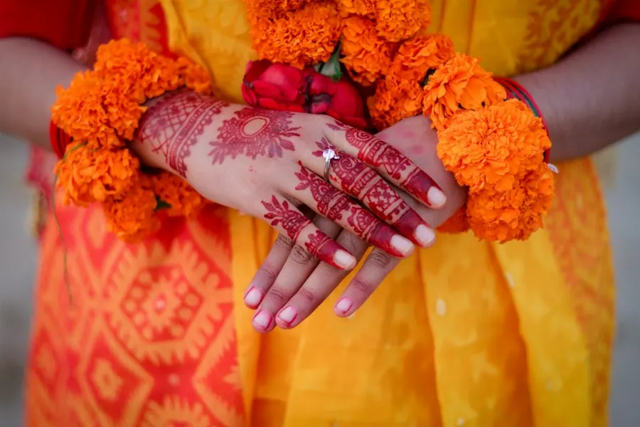 Henna-decorated hands with marigold garlands at a wedding